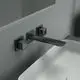 Wandarmatur in mattem Schwarz mit eckigen Rosetten von Ideal Standard. Die Armatur hat einen langen, flachen Auslauf und ist an einer grauen Wand montiert.
